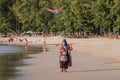 Thai women selling flying kite toy in form and color of predator bird walks along seashore on tourist beach. BANG THAO, PHUKET