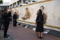 Thais in black mourning clothes are photographed at a wall with the image of the dead king Bhumibol Adulyadej. A fragment of funer
