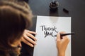 Thank you. Calligrapher Young Woman writes phrase on white paper. Inscribing ornamental decorated letters. Calligraphy Royalty Free Stock Photo