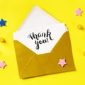 Thank you card in a golden envelope, overhead square shot on a yellow background Royalty Free Stock Photo