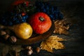 Thanksgiving composition with autumn fruit in wooden plate with maple leaves. Pumpkin and grapes vintage still life scene.