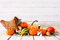 Thanksgiving cornucopia filled with autumn vegetables and pumpkins against white wood