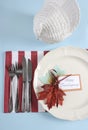 Thanksgiving dining table place setting in modern pale blue, red and white theme - vertical.