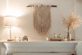 Thanksgiving home decor - white wooden fireplace with wall macrame, cream and beige pumpkins, pine cones garland and rustic dry