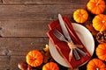 Thanksgiving table setting with pumpkins and orange napkin, fork and knife on a plate against rustic wood