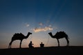 Thar desert, Rajasthan, India- 15.10.2019 : Silhouette of two cameleers and their camels at sand dunes. Cloud with setting sun, Royalty Free Stock Photo