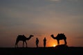 Thar desert, Rajasthan, India- 15.10.2019 : Silhouette of two cameleers and their camels at sand dunes. Cloud with setting sun, Royalty Free Stock Photo