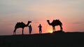 Thar desert, Rajasthan, India- 15.10.2019 : Silhouette of two cameleers and their camels at sand dunes. Cloud with setting sun, Royalty Free Stock Photo