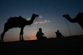 Thar desert, Rajasthan, India- 15.10.2019 : Silhouette of two cameleers and their camels at sand dunes. Cloud with setting sun, Royalty Free Stock Photo