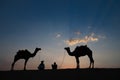 Thar desert, Rajasthan, India- 15.10.2019 : Silhouette of two cameleers and their camels at sand dunes. Cloud with setting sun, Royalty Free Stock Photo