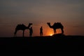 Thar desert, Rajasthan, India- 15.10.2019 : Silhouette of two cameleers and their camels at sand dunes. Cloud with setting sun, Royalty Free Stock Photo