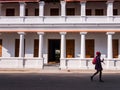 A man in silhouette walking past the exterior facade of a white colonial building