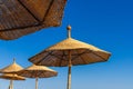 Thatched beach umbrella against the blue sky, hot sun and sea horizon. Wicker umbrellas on the beach. Rattan fungi from the sun on