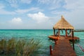 Thatched hut at the end of a pier jutting out into the blue water of the Bacalar lagoon