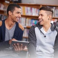 Thats pretty funny. two young men laughing while using a digital tablet in the university library. Royalty Free Stock Photo