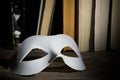 Theater concept. White classical carnival mask on books background with vintage hourglass on wooden table