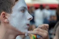 Theatrical performance on the streets. A female hand applies white makeup to the face of a teenager boyfriend. The boy in the Royalty Free Stock Photo