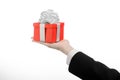 The theme of celebrations and gifts: a man in a black suit holding a exclusive gift wrapped in red box with white ribbon and bow,