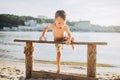 The theme is a child and summer beach vacation. A small Caucasian boy climbs up on a wooden bench on the river bank in a sunny sum