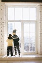 Theme Christmas morning. Two baby Caucasian boy and girl brother and sister standing with backs on window front of large box in em Royalty Free Stock Photo