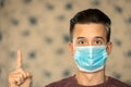 Theme of coronavirus and safety. Young man with emotions of confusion, in a blue mask from a virus shows thumb up. Place for an