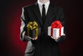 Theme holidays and gifts: a man in a black suit holding two exclusive gift packaged in a black box with gold ribbon and bow and a