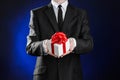Theme holidays and gifts: a man in a black suit holds an exclusive gift in a white box wrapped with red ribbon and bow on a dark Royalty Free Stock Photo