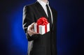 Theme holidays and gifts: a man in a black suit holds an exclusive gift in a white box wrapped with red ribbon and bow on a dark Royalty Free Stock Photo