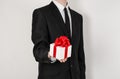 Theme holidays and gifts: a man in a black suit holds an exclusive gift in a white box wrapped with red ribbon and bow isolated on Royalty Free Stock Photo