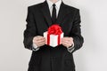 Theme holidays and gifts: a man in a black suit holds an exclusive gift in a white box wrapped with red ribbon and bow isolated on Royalty Free Stock Photo