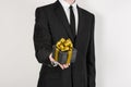 Theme holidays and gifts: a man in a black suit holds exclusive gift wrapped in a black box with gold ribbon and bow isolated on Royalty Free Stock Photo