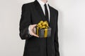 Theme holidays and gifts: a man in a black suit holds exclusive gift wrapped in a black box with gold ribbon and bow isolated on Royalty Free Stock Photo