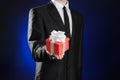 Theme holidays and gifts: a man in a black suit holds exclusive gift wrapped in red box with white ribbon and bow on a dark blue Royalty Free Stock Photo