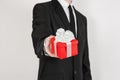 Theme holidays and gifts: a man in a black suit holds exclusive gift wrapped in red box with white ribbon and bow isolated on a Royalty Free Stock Photo