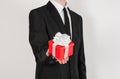 Theme holidays and gifts: a man in a black suit holds exclusive gift wrapped in red box with white ribbon and bow isolated on a Royalty Free Stock Photo