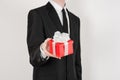 Theme holidays and gifts: a man in a black suit holds exclusive gift wrapped in red box with white ribbon and bow isolated on a Royalty Free Stock Photo