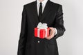 Theme holidays and gifts: a man in a black suit holds exclusive gift wrapped in red box with white ribbon and bow isolated on a Royalty Free Stock Photo