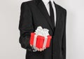 Theme holidays and gifts: a man in a black suit holds exclusive gift wrapped in red box with white ribbon and bow isolated on a Royalty Free Stock Photo