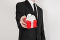 Theme holidays and gifts: a man in a black suit holds exclusive gift wrapped in red box with white ribbon and bow isolated on a Royalty Free Stock Photo