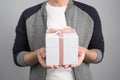 Theme holidays and gifts: a man holds an exclusive gift in a white box wrapped with pink ribbon and bow isolated on a gray Royalty Free Stock Photo