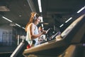 Theme sport and music. A beautiful Caucasian woman running in gym on treadmill. On head big white headphones, the girl listens to Royalty Free Stock Photo