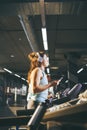 Theme sport and music. A beautiful Caucasian woman running in gym on treadmill. On head big white headphones, the girl listens to Royalty Free Stock Photo