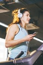 Theme sport and music. A beautiful Caucasian woman running in gym on treadmill. On head big white headphones, the girl listens to Royalty Free Stock Photo