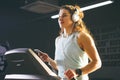 Theme sport and music. A beautiful Caucasian woman running in gym on treadmill. On head big white headphones, the girl listens to Royalty Free Stock Photo