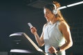 Theme sport and music. A beautiful Caucasian woman running in gym on treadmill. On head big white headphones, the girl listens to Royalty Free Stock Photo