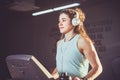 Theme is sport and music. A beautiful inflated woman runs in the gym on a treadmill. On her head are big white headphones, the gir Royalty Free Stock Photo