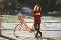 Theme tourism on bicycle and modern technology. Beautiful young caucasian woman stands near red retro bicycle on riverside river R Royalty Free Stock Photo