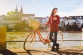 Theme tourism on bicycle and modern technology. Beautiful young caucasian woman stands near red retro bicycle on riverside river R Royalty Free Stock Photo