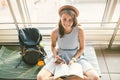 Theme of tourism and travel of young student. Beautiful young caucasian girl in dress and hat sits on floor tourist rug inside Royalty Free Stock Photo