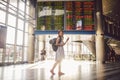 Theme travel and tranosport. Beautiful young caucasian woman in dress and backpack standing inside train station or terminal looki